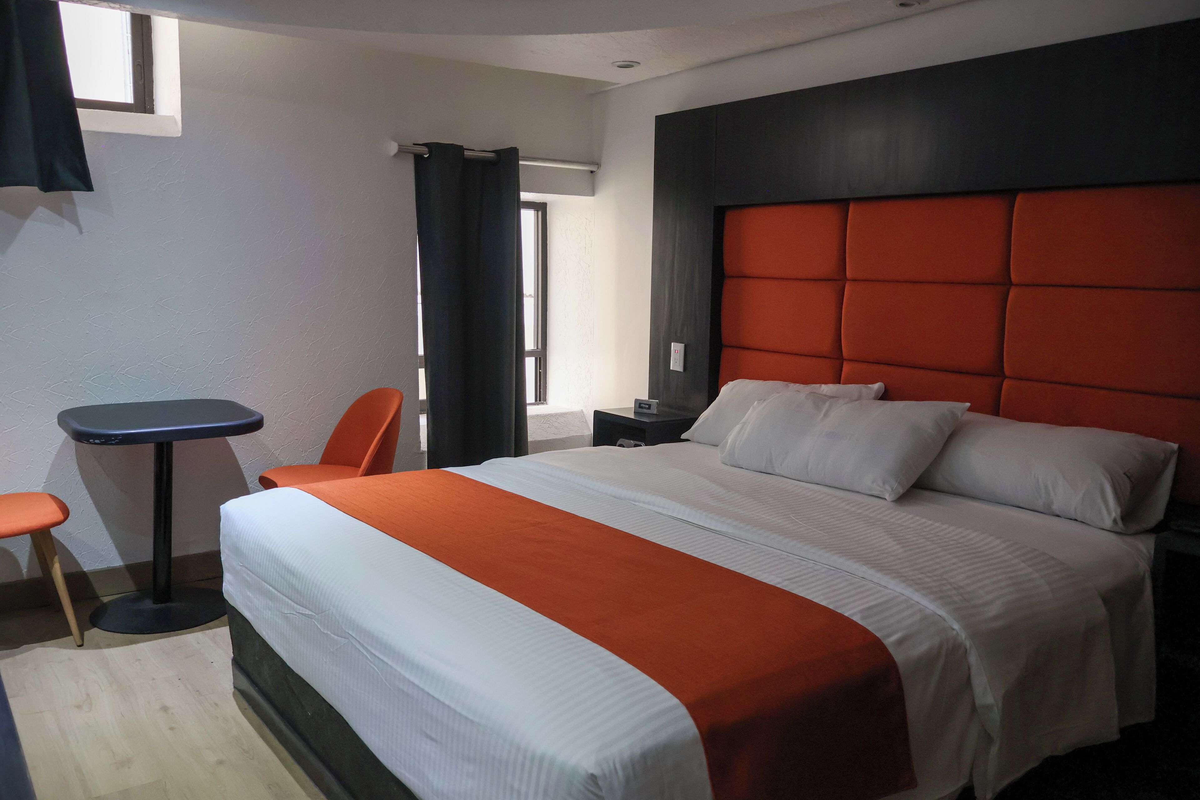 Ein Hotelzimmer mit einem großen Bett, einer orangefarbenen Akzentwand, einem kleinen Tisch und einem Stuhl.