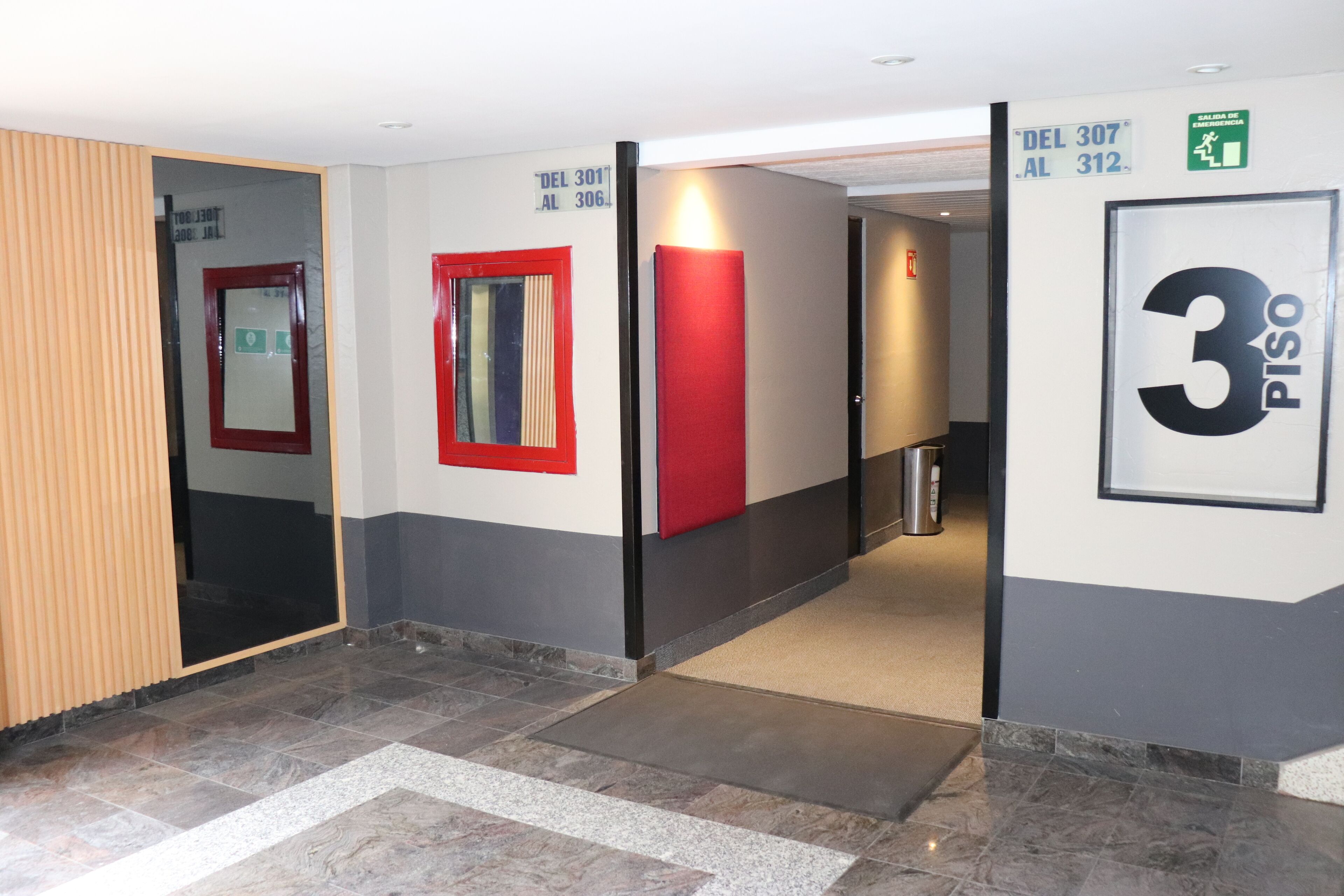 Un pasillo con piso de baldosas, pared roja y un cartel que indica las habitaciones 307 y 312.