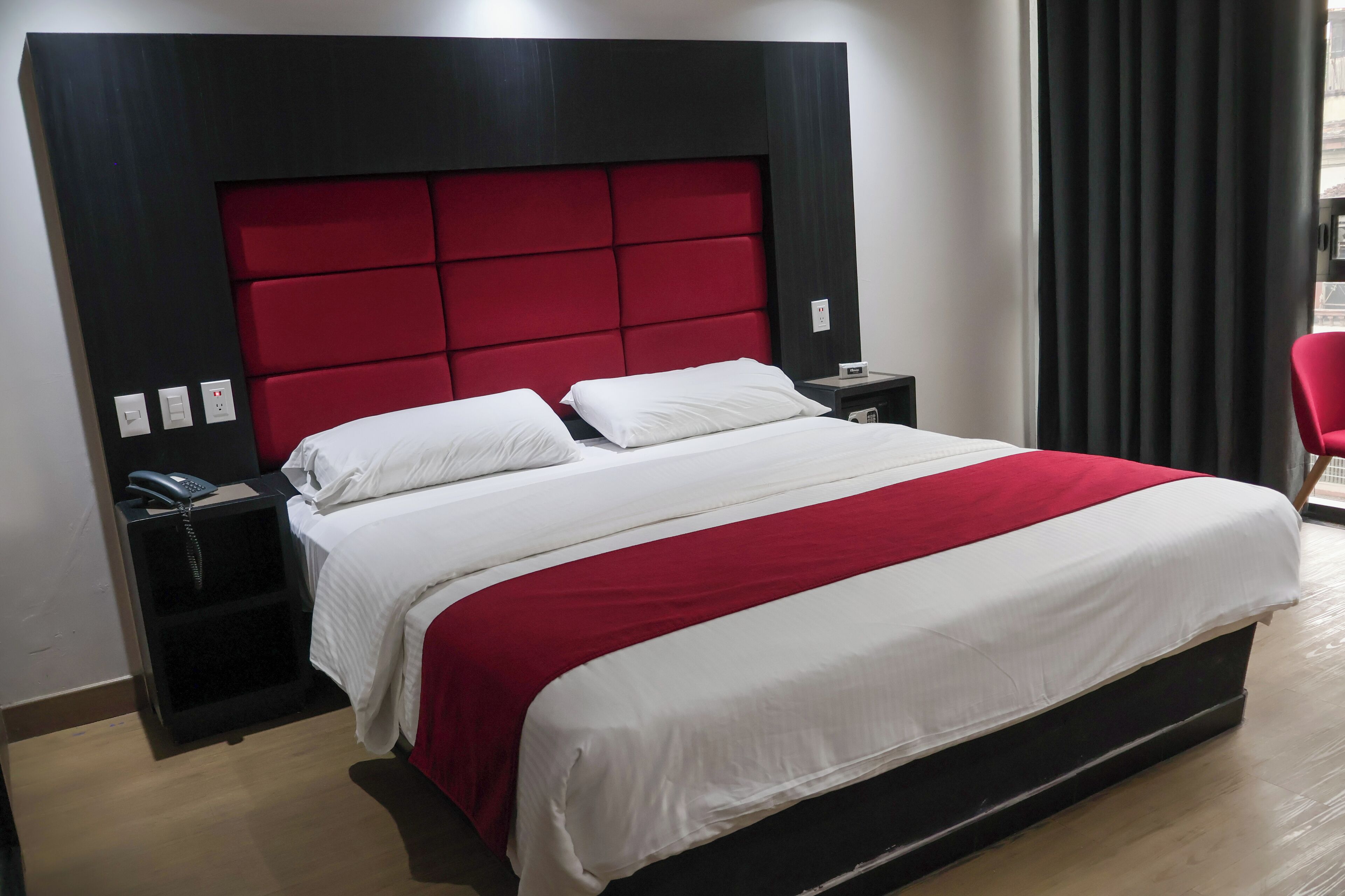 Ein Hotelzimmer mit einem großen Bett, einem roten Kopfteil, einem Nachttisch mit Telefon und einem roten Sessel.