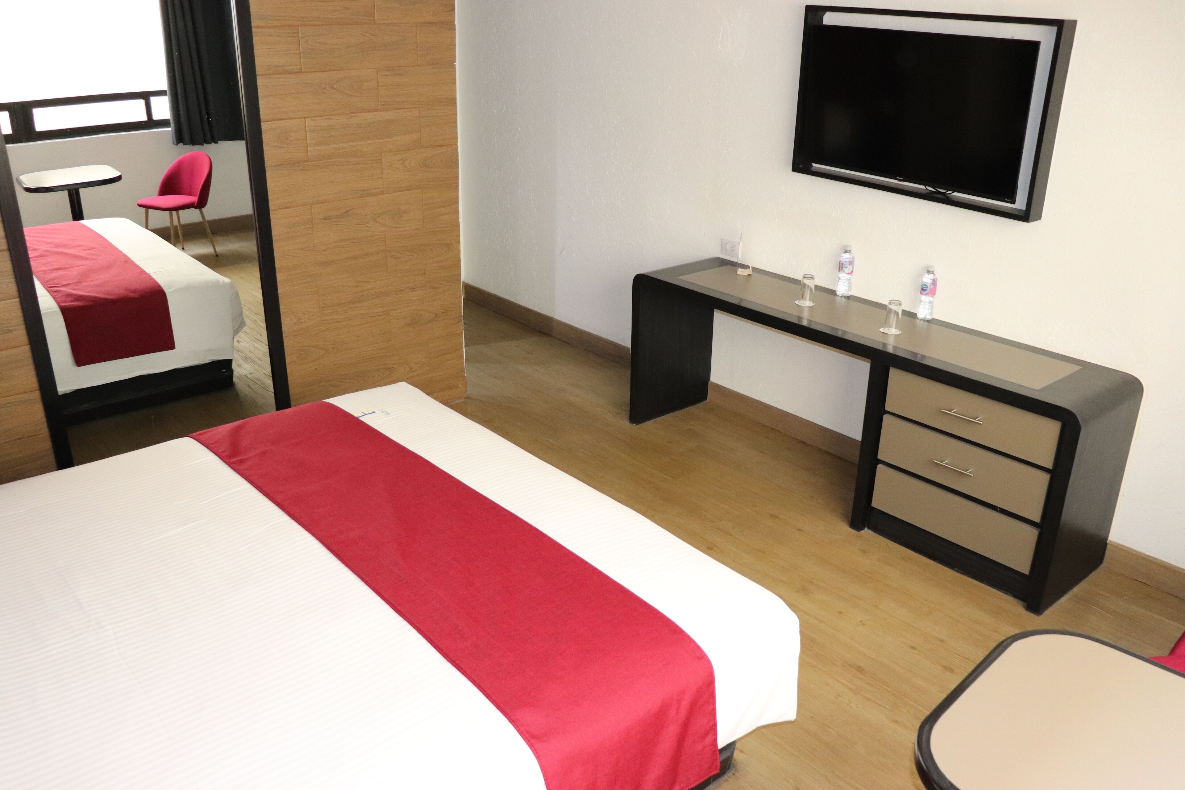 Una habitación de hotel con cama, escritorio, silla, televisor y una mesita.