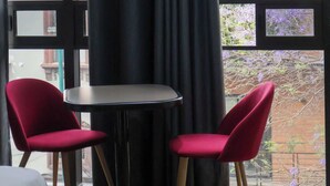 A room with a large window, a round table, and two red chairs.