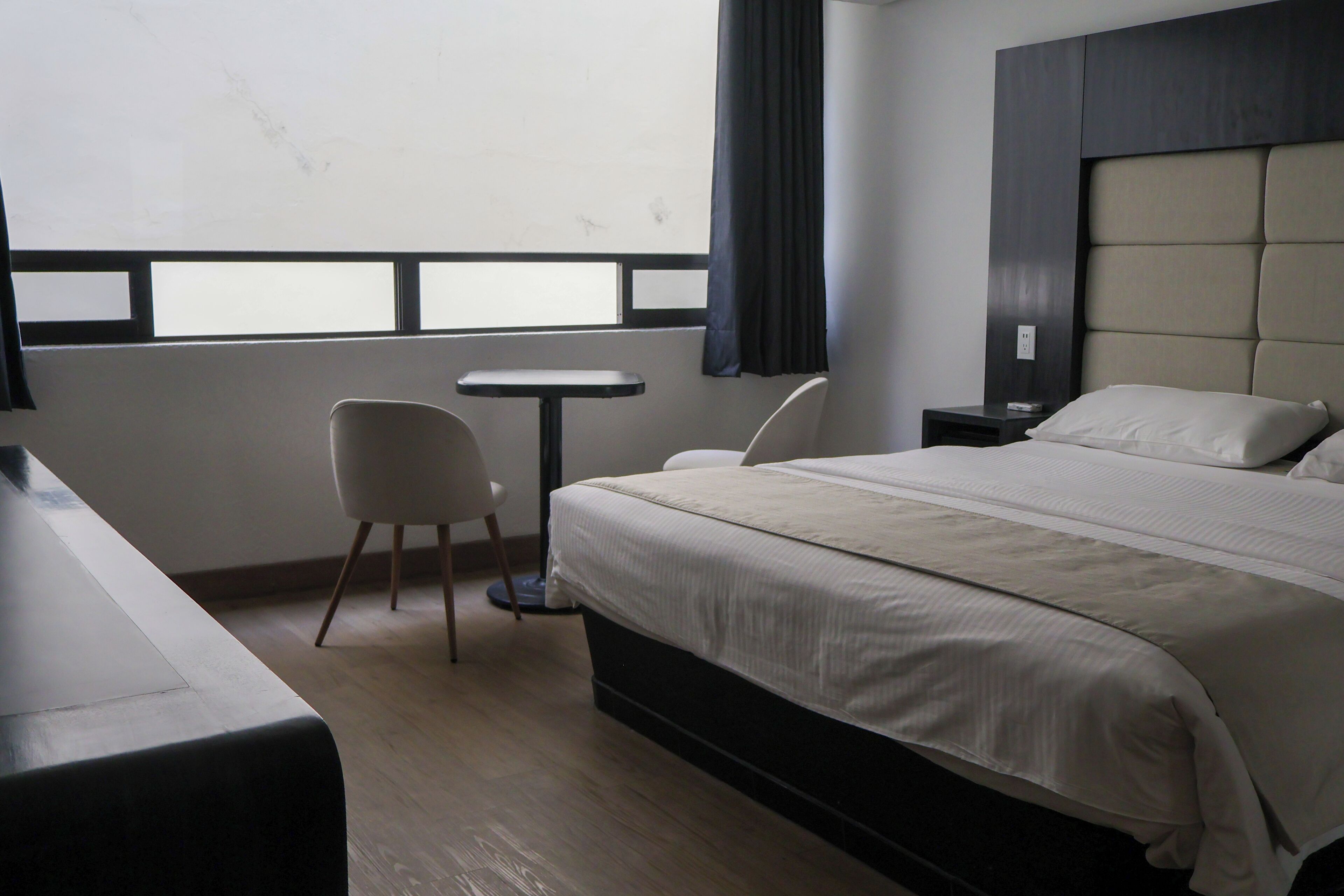 Une chambre d’hôtel avec un lit, une petite table, une chaise et une fenêtre avec des rideaux.