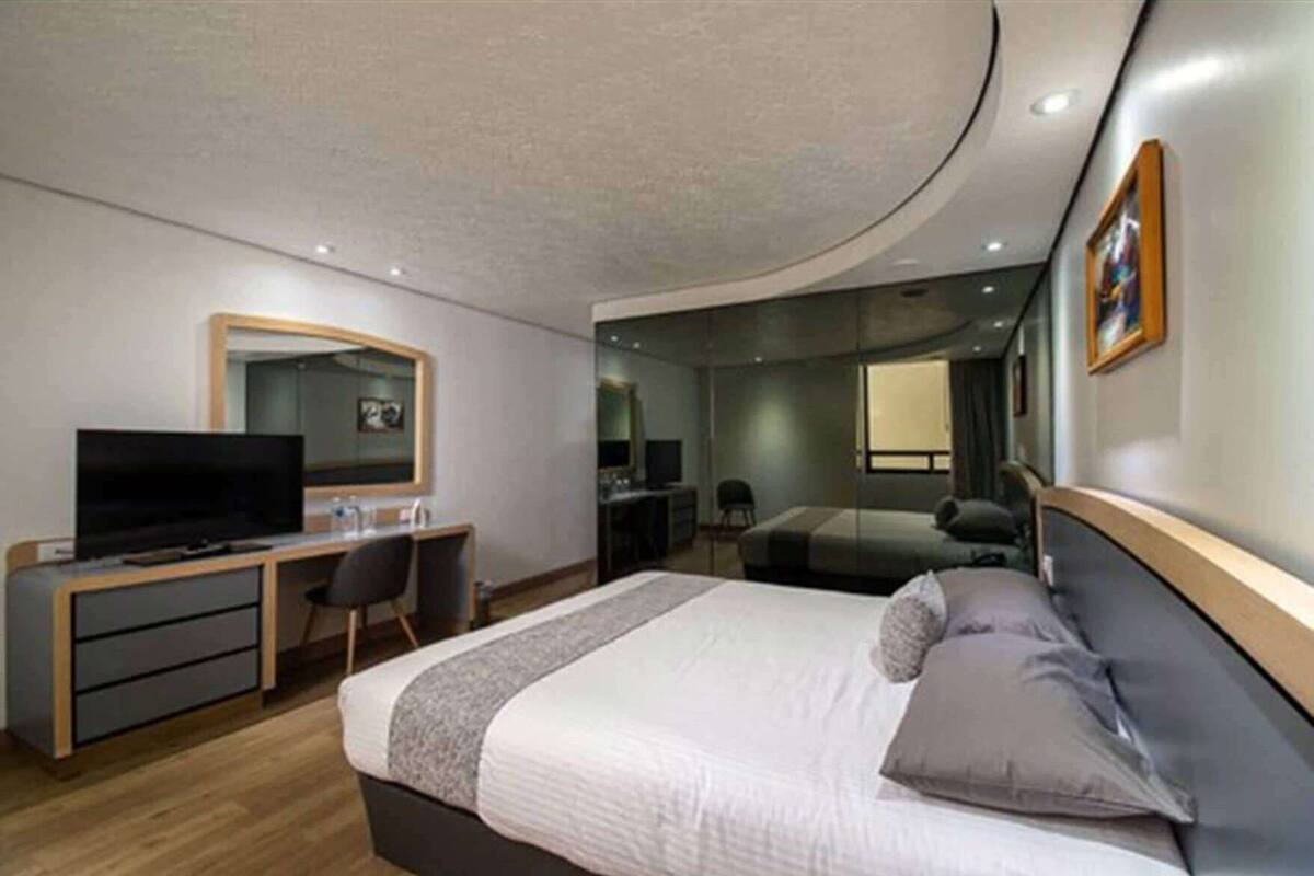 Una habitación de hotel moderna con cama, escritorio, televisor y un espejo grande.