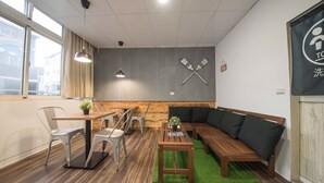 Ein modernes Interieur mit einer Holzbank, einem kleinen Tisch und einem Sofa. Zwei Pendelleuchten, ein Fenster mit Vorhängen und ein an der Wand befestigtes Schild sind vorhanden.