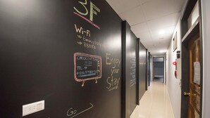 Ein Flur mit einer schwarzen Wand, auf der Kreideanschriften zu sehen sind, darunter Informationen zu WLAN, eine Auscheckzeit und eine Telefonnummer.