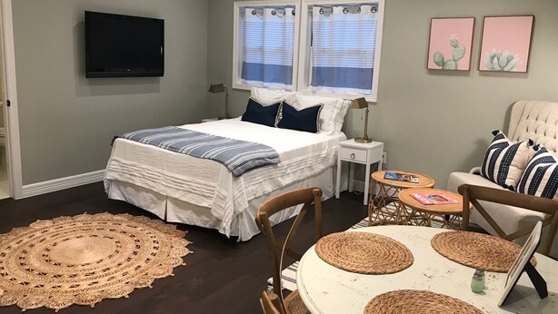 A bedroom with a bed, bedside tables, a TV, a chair, a table, and two windows with curtains. - Carriage House in Tarrytown - Central Austin, New in 2018 (Austin)