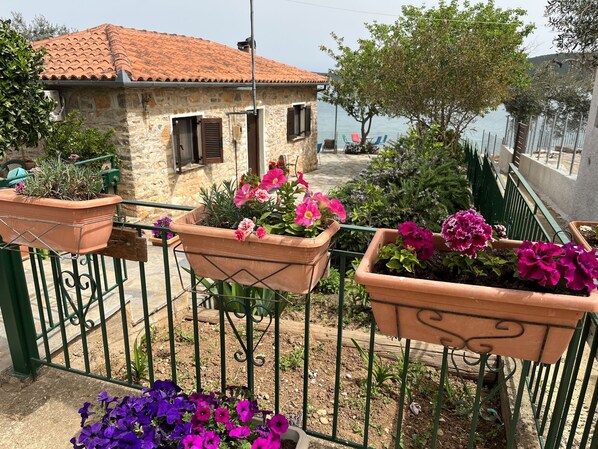 Une maison en pierre avec des tuiles en terre cuite, un balcon orné de pots de fleurs et une vue sur la mer.