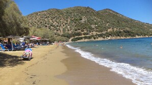 Ein Strand mit badenden und sonnenden Menschen, einem klaren Himmel und einem Berg im Hintergrund.