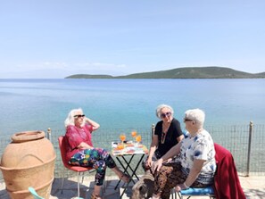 Trois personnes sont assises à une table, d’où l’on a une vue sur la mer et une île lointaine.