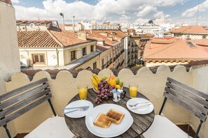 A balcony table with breakfast items, a city view, and a tiled roof. - Waou Plaza Mayor I - Alquiler Corta Duración (Madrid)