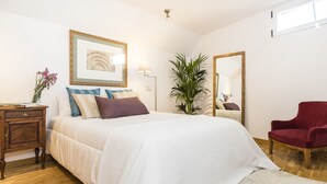 Een slaapkamer met een bed, nachtkastje, spiegel, een bloempot en een rode stoel.