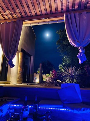 An outdoor seating area with a view of the night sky, a wooden pergola, and a well-lit patio.