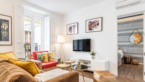 A modern living room with a red sofa, a brown sofa, a TV, and a small table with a lamp. - Waou Sol es MIA - Corta Duración (Madrid)