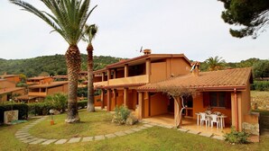 Una casa a due piani con tetto in tegole, un patio con sedie e un giardino con palme.
