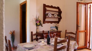 Zona pranzo con tavolo apparecchiato per quattro, una sedia in legno, un vaso con fiori e una bottiglia di vino.