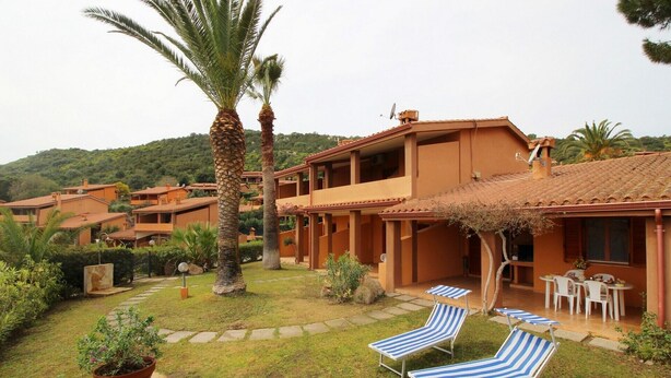 Un hotel con diversi piani, area relax esterna con poltrone a righe e un giardino con palme.