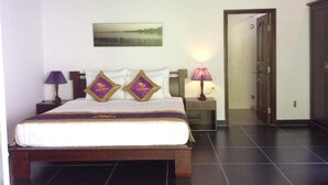 Un letto rifatto con una coperta bianca e viola, due cuscini decorativi, un comodino con una lampada e un quadro appeso al muro.