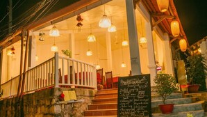 Un ristorante con un'area salotto esterna coperta, una scala che conduce all'ingresso e una lavagna con il menu che propone diversi piatti.