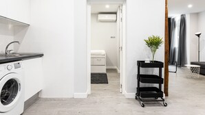 Een moderne keuken met een wasmachine, een kleine tafel met een plant en een zwarte trolley.