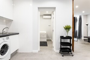 Une cuisine moderne équipée d’un lave-linge, d’une petite table avec une plante et d’un chariot noir.