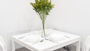 Un tavolo bianco apparecchiato con piatti, posate e un vaso con fiori gialli.