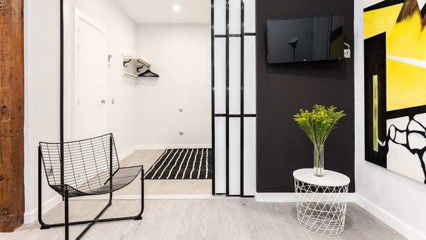 A modern interior with a black and white color scheme, a television mounted on the wall, a black chair, and a small round table with a vase of flowers.