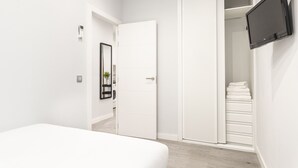 A bedroom with a bed, a white wardrobe, a television mounted on the wall, and a door leading to a bathroom.