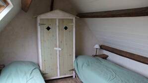 Une petite pièce rustique, avec une armoire en bois, deux lits simples et un plafond en pente.