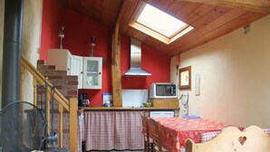 Une cuisine compacte équipée d’un four à micro-ondes, d’une cuisinière et d’un mur rouge. Un escalier en bois mène à une mezzanine dotée d’un puits de lumière.