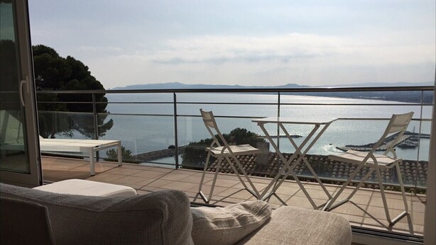 Un balcon avec un canapé et deux fauteuils, donnant sur une étendue d’eau et sur des montagnes lointaines.