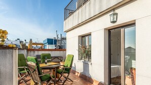 Eine Terrasse mit Tisch, Stühlen, einer Pflanze im Topf und Blick auf die Stadtlandschaft.