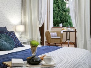 Enjoy a peaceful retreat with a neatly made bed, a tea service, and a view of lush greenery.