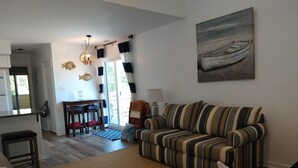 A living room with a striped sofa, a dining area with a table and chairs, a kitchen area, and a large window with curtains. - COMPLETELY RENOVATED! Immaculately clean and new. See new photos! (Surfside Beach)