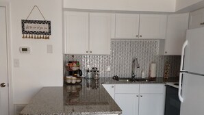 A kitchen with white cabinets, a granite countertop, a blue rug with a starfish design, and a hanging sign that reads "Let the sea set you free". - COMPLETELY RENOVATED! Immaculately clean and new. See new photos! (Surfside Beach)