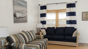 A living room with a striped sofa, a dark sofa, a lamp, a ceiling fan, and a painting of a boat. - COMPLETELY RENOVATED! Immaculately clean and new. See new photos! (Surfside Beach)