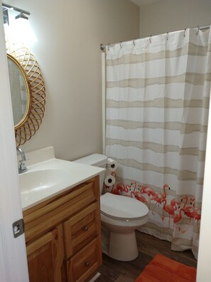 A bathroom with a white sink, wooden vanity, toilet, and a striped shower curtain. - COMPLETELY RENOVATED! Immaculately clean and new. See new photos! (Surfside Beach)