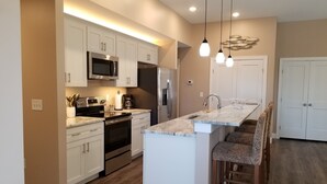 A modern kitchen with white cabinetry, stainless steel appliances, a marble countertop, and pendant lighting. - Walk to beach! Cottage perfect for families. (Kill Devil Hills)