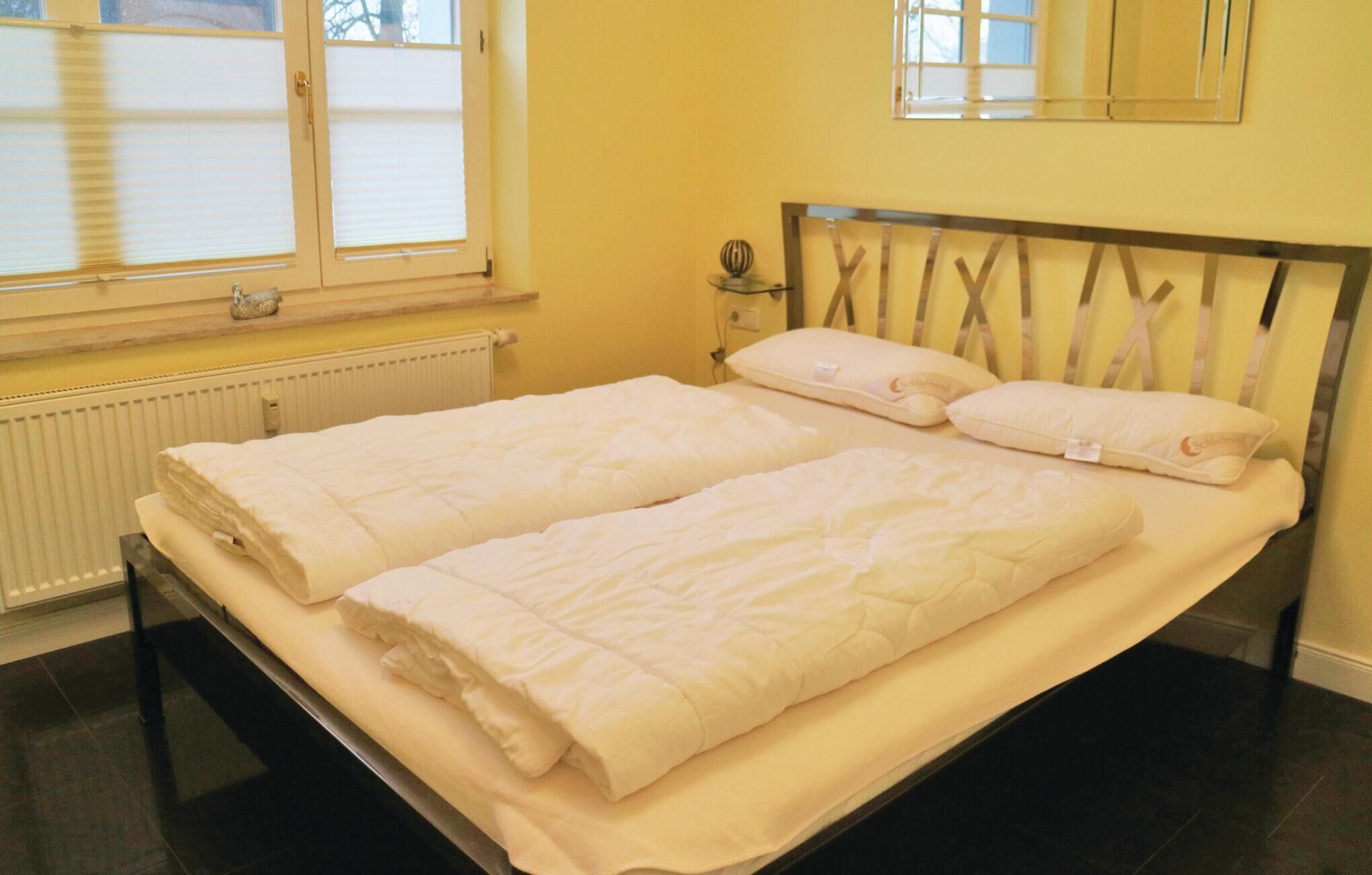 Una cama doble con dos almohadas, una mesita de noche con lámpara y una ventana con persianas.