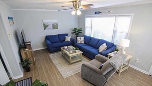 Ein Wohnzimmer mit blauem Sofa, einem grauen Sessel, einem Holztisch und einem Deckenventilator.