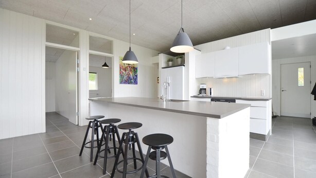 Una cocina moderna con armarios blancos, una isla central con taburetes y luces colgantes, además de un refrigerador.