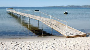 Un muelle de madera se extiende sobre aguas tranquilas, con una playa de arena al final.