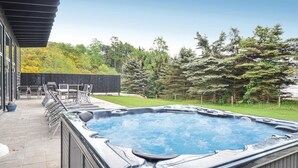 Un jacuzzi en un patio trasero con un área de terraza, mobiliario exterior y una valla de madera.