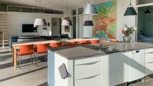 Una cocina moderna con una isla central, un área de comedor con sillas naranjas y un mapa grande en la pared.