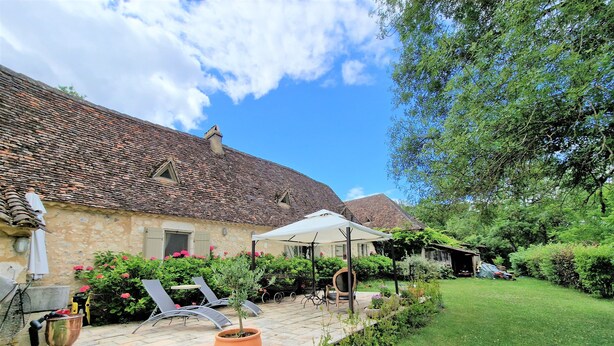 Un bâtiment rustique en pierre, doté d’un toit en tuiles, d’une terrasse pavée avec des meubles d’extérieur et d’un jardin bien entretenu.