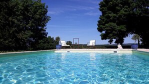 Une piscine d’un bleu éclatant, entourée d’arbres, avec des chaises longues et une vue sur le paysage.