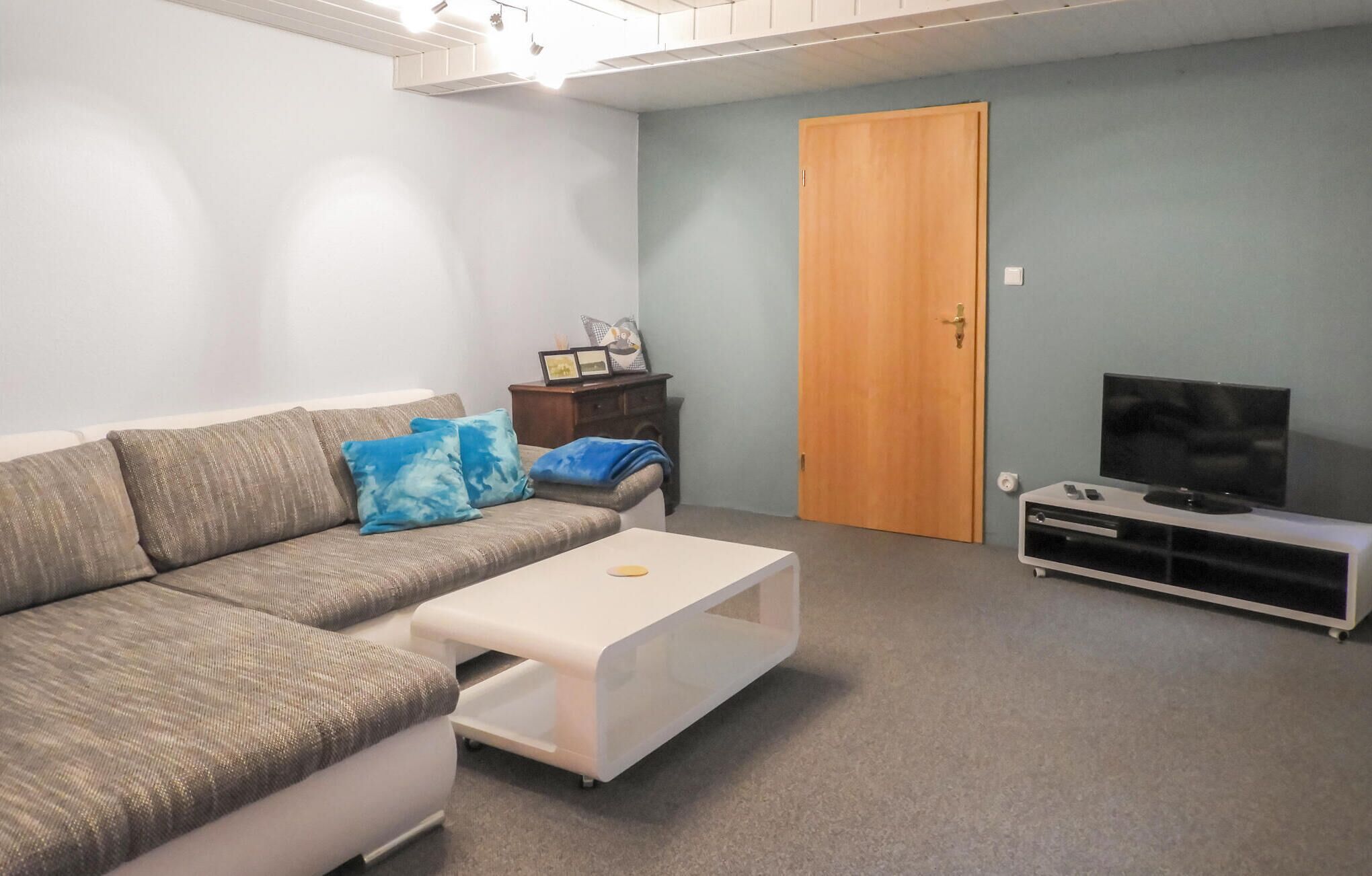A living room with a sofa, a coffee table, a TV stand, and a door.