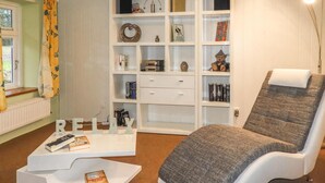 Un soggiorno con una libreria bianca, una poltrona grigia e un tavolino da caffè con libri.