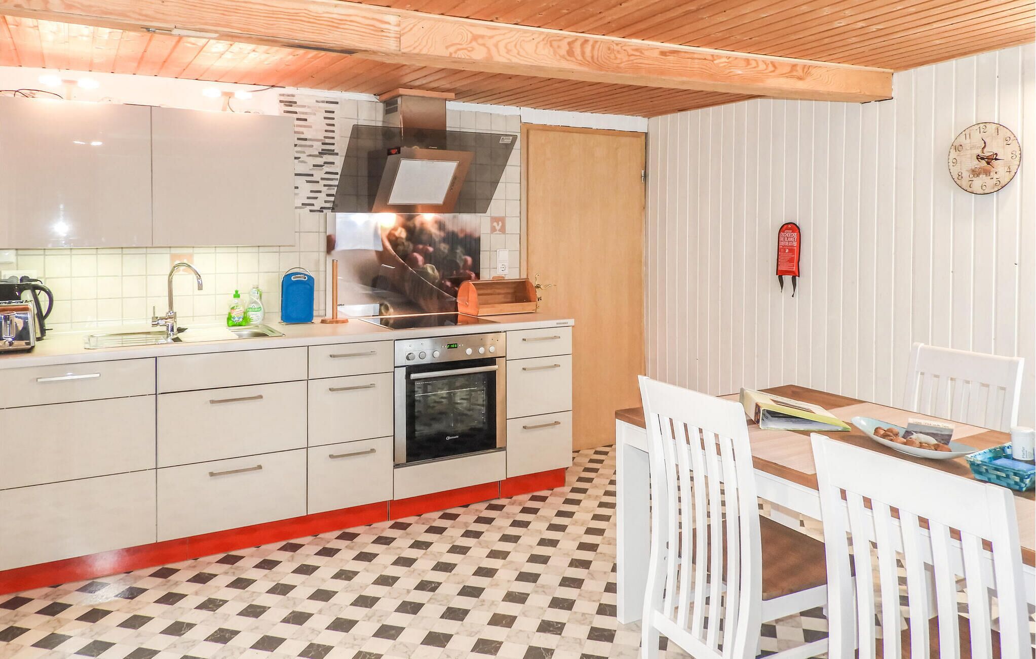 Una cocina con armarios blancos, horno con marco rojo, un lavamanos y piso a cuadros.