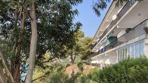 A multi-story building with balconies, surrounded by lush greenery and trees.