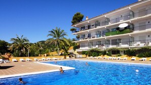 A swimming pool with lounge chairs and a multi-story building in the background.